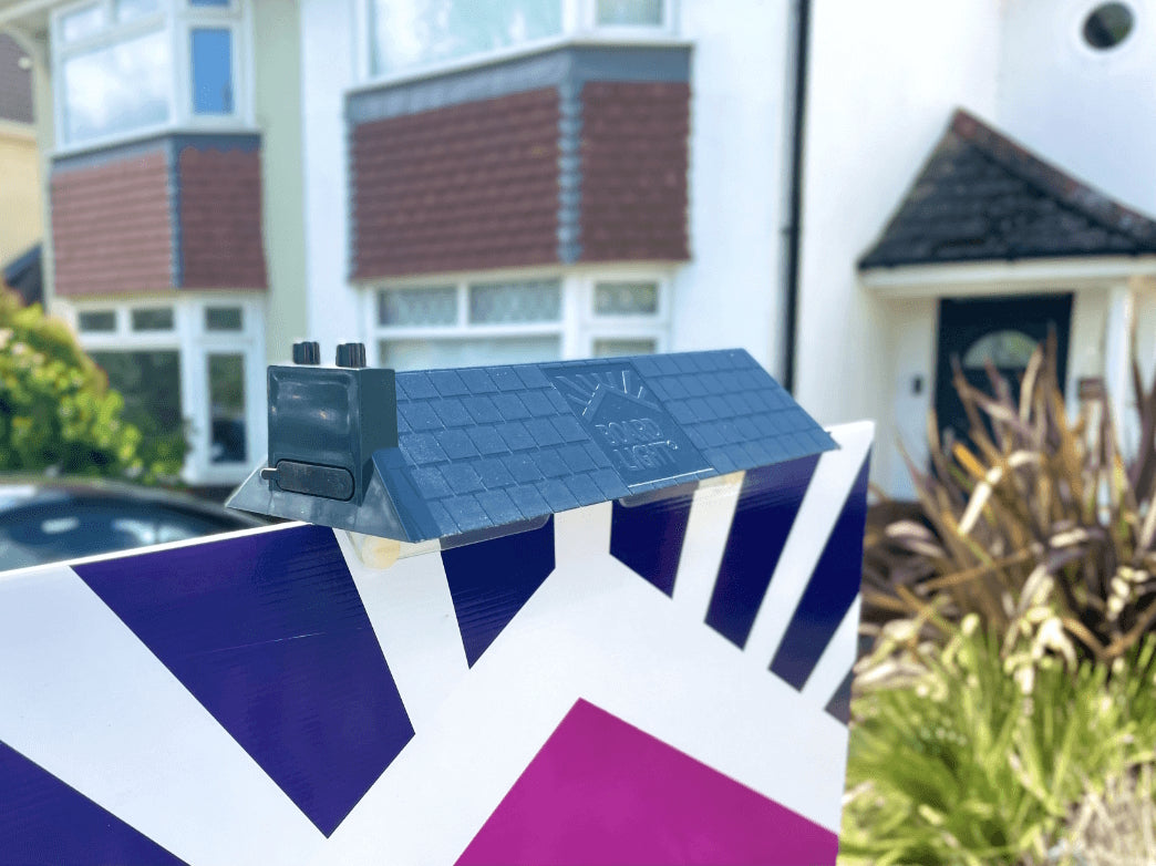 Small model of a house - 'Boardlight' - on a for sale board in front of a residential building.